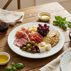 Platter of assorted meats, cheeses, and crackers on a wooden table with glasses of red wine.