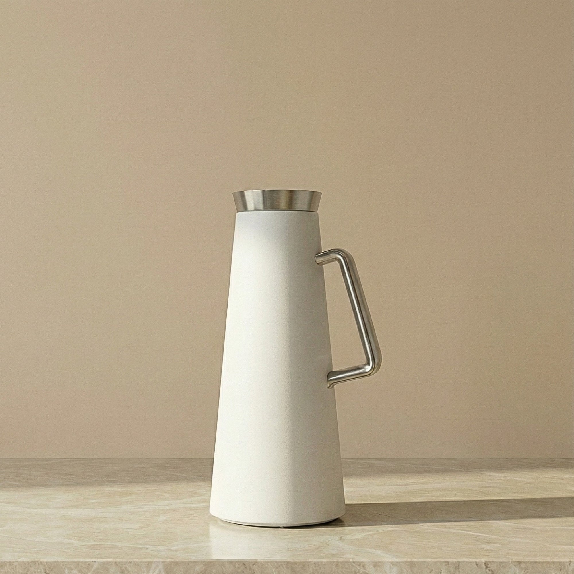 White pitcher with silver handle and lid on a wooden surface with a beige background