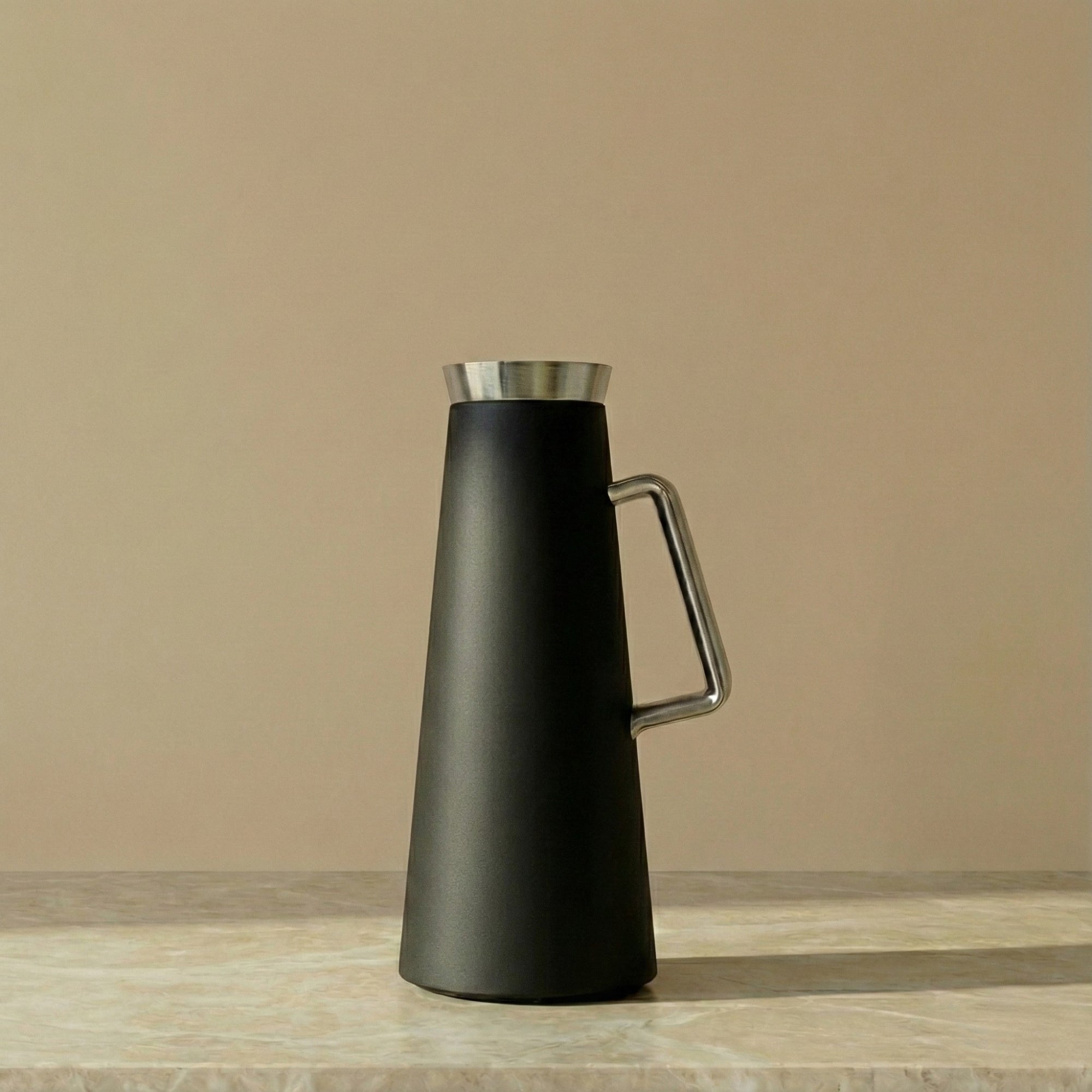 Black thermos with silver lid and handle on a beige background
