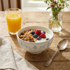 Bowl of cereal with yogurt, berries, and a glass of orange juice on a wooden table.