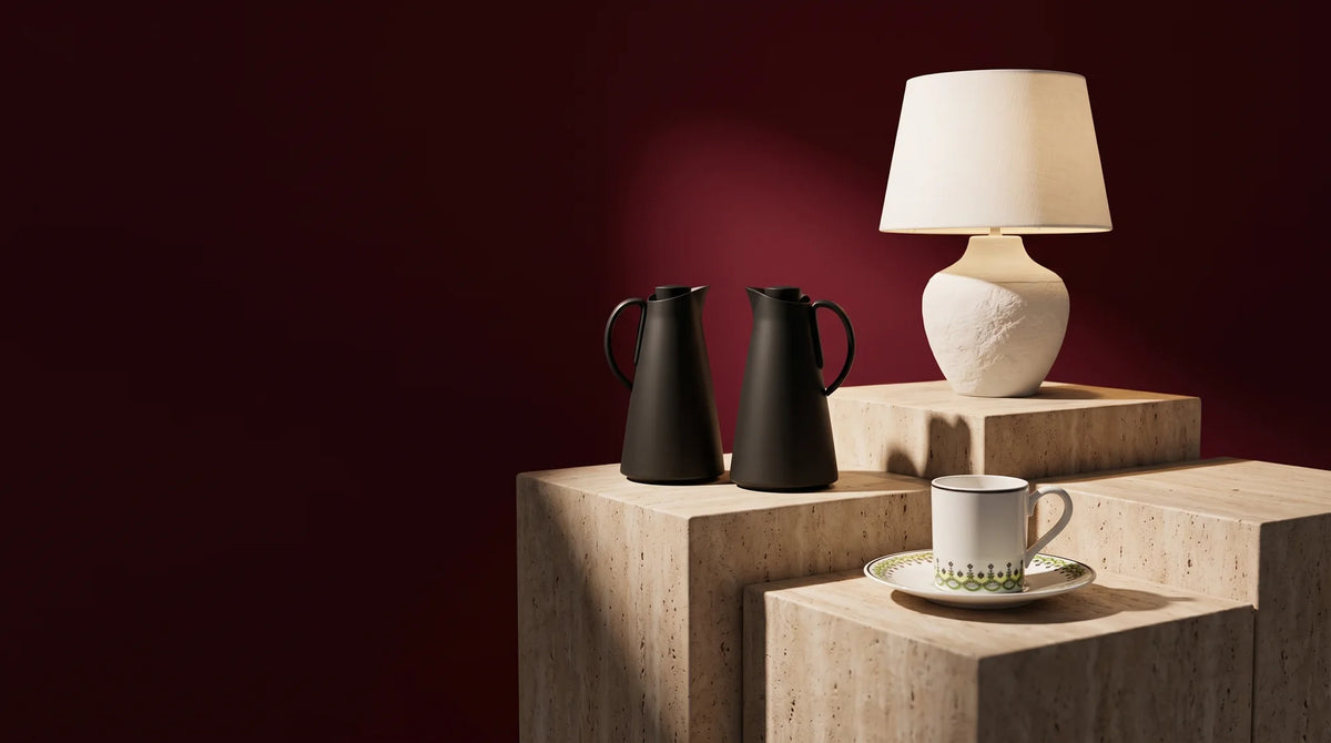 Luhpar black Adaman jugs, white Aria lamp and patterned coffee cups on travertine against burgundy