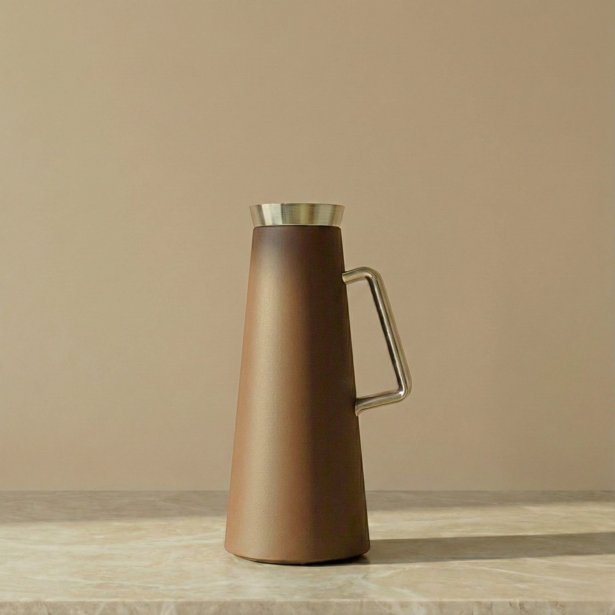 Brown  pitcher with silver handle and trim on a beige background